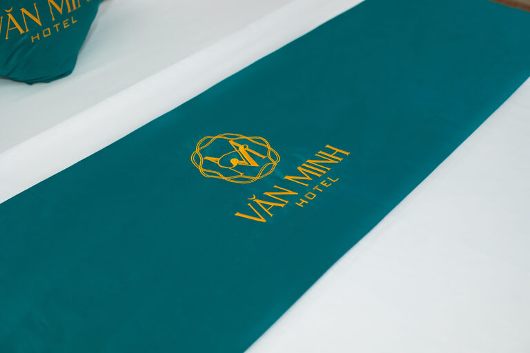 Khăn trải giường màu xanh ngọc thêu logo Văn Minh Hotel màu vàng đồng